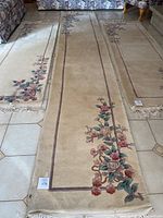 Full view of long oriental carpet runner laid out showing floral and border design against beige background.