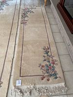 Full length view of the beige oriental runner on tiled floor showing floral embroidery and fringes.