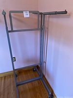Overall front view of the gray metal adjustable hanging rack with caster wheels on hardwood floor and light pink wall.