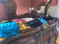 Photo showing an assortment of folded scarves including a bright blue fringed scarf and a multicolored patterned scarf on a wooden dresser.