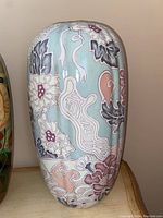 Side view of large porcelain vase with light blue background and floral and abstract pastel designs.