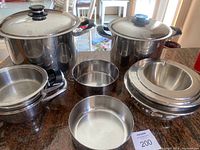 Overview of two lidded stock pots, saucepan, round pan and nested bowls on countertop