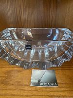 Clear Rogaska crystal bowl displayed on a wood shelf with label showing brand name and origin (Slovenia).
