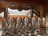 Front row of eight silver-tone flutes on mirrored shelf; mirror creates reflection of back row