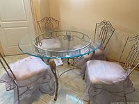 Full view of the round glass top table with four metal chairs arranged around it.