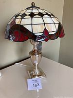 Full view of the table lamp showing the chrome base and Tiffany-style mushroom stained glass shade in white, red, and brown colors.