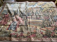 Full view of vintage woven tapestry mural showing 18th century garden scene with three figures, floral borders, and architectural elements