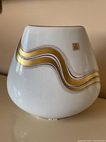 Front and side view of white ceramic vase with gold and black wavy lines and Birks emblem sticker visible