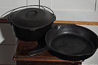 Two cast iron cookware pieces placed on a wooden surface, showing both skillet and Dutch oven with lid and bail handle.