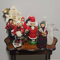 Various Christmas figures displayed on a wooden table including Santa, carolers, nutcracker, and snowmen.