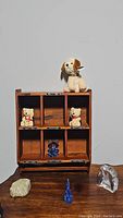 Wooden shelf with compartments and ceramic dog figurine on top, ceramic bears inside, and three glass figurines on wood surface in front