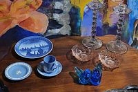Photo showing the assortment of decorative items: blue ceramic cup and saucer, commemorative blue and white plate, small blue dish, two small blue glass birds, two cut glass bowls, and two clear glass twisted stem candlesticks.
