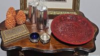 Overview of assorted decorative pieces on a wooden surface, showing candles, a red platter, a decorative box, and small bowls.