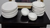 White dish set with stacked dinner plates, side plates, and bowls arranged on a dark table.