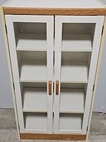 Front view of white display cabinet with oak trim, glass double doors, and wooden handles.