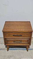 Front view of the mid century two drawer nightstand showing wood grain finish and metal handles