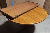 Photo showing two leaves separated from round table top, highlighting the table extension mechanism and the wood grain surface