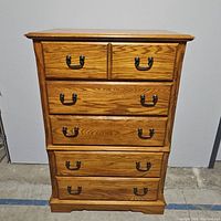 Front view of wooden tall chest with five drawers, showing metal handles and wood grain finish.