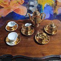 Full view of tea set showing teapot, sugar bowl, creamer, and three cups with saucers on a wooden surface.