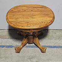 Front view of vintage oak pedestal side table showing the wooden top and claw feet base.