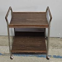 Front view of the vintage tea cart showing two wooden shelves and metal frame with wheels.