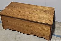 Front and top view of the wooden bench showing wood grain pattern, simple curved detail on front panel, and boxy rectangular shape.