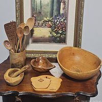 Photo showing all wooden kitchen items arranged on a wooden table including bowls, spoons, mortar and pestle, and trivet.