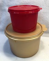 Photo showing stacked large beige bowl with beige lid and smaller red bowl with red lid on top