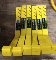 Six yellow metal roofing brackets laid flat side by side showing front mounting faces and hooks.