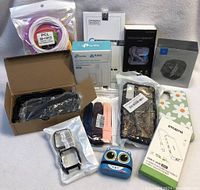 Full lot showing various electronics including smartwatches, smart plugs, wireless headset, protective cases, kids Bluetooth speaker, and USB-C hub with original packaging.