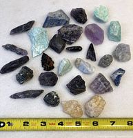 Topdown photo showing the full lot of rough stones and crystals arranged on a light background with a measuring tape for scale