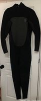 Front view of the full wetsuit hanging on a door, showing black body with grey chest panel and textured side sleeves.