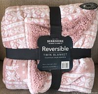 Folded pink and white patterned reversible Berkshire twin blanket with packaging label and black strap.