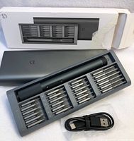 Electric precision screwdriver with bits and USB charger in gray case, box showing partially torn packaging