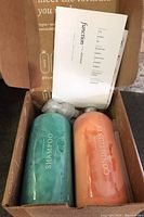 Photo showing open box with teal shampoo and orange conditioner bottles along with pump dispensers and a brochure inside the box.