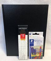 Black Arteza sketchbook standing with box of 12 Arteza pencils and box of Staedtler 12 oil pastels in front
