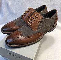 Pair of brown men's dress shoes angled side view on Kenneth Cole Reaction shoebox showing leather and fabric material details.