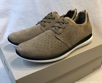 Side angle view showing the taupe perforated upper and black and white sole on box background.