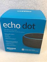 Front and top view of the sealed Amazon Echo Dot in blue retail box showing product name, image, and Alexa commands.