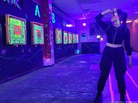 Indoor axe throwing lanes illuminated with blacklights and neon target boards, showing a person holding an axe ready to throw.