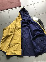 Adult reversible rain coat laid flat showing yellow exterior and navy blue interior with pockets and hood