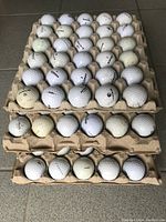Three egg trays each filled with multiple white golf balls of various brands showing signs of wear.