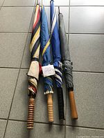 Three golf umbrellas closed, showing different handle types and canopy colors