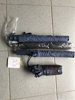 Four folded umbrellas on tiled floor with plastic covers, varying shades of blue and black.