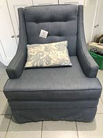 Front view of blue lounge chair with decorative pillow showing fabric and tufting detail.