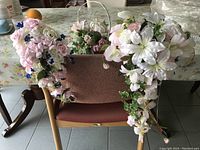 Set of bridal silk flower bouquets and matching basket displayed on chair with table background.