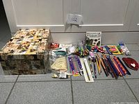 Full lot overview including decorative storage box, model ship kits, gel pens, pencils, erasers, sticky notes, and ruler on tiled floor.