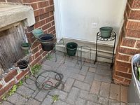 Set of four iron wrought plant stands arranged outside against a brick wall and door, showing the full lot and scale with plant pots (pots not included in sale).