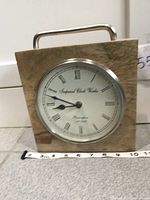 Front view of rustic wood square tabletop clock with metal handle on top, showing natural wood grain and round white clock face.