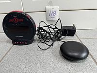 Sonic Bomb alarm clock with vibrating pad and tangled cable, connected to power plug, displayed on a tiled surface.